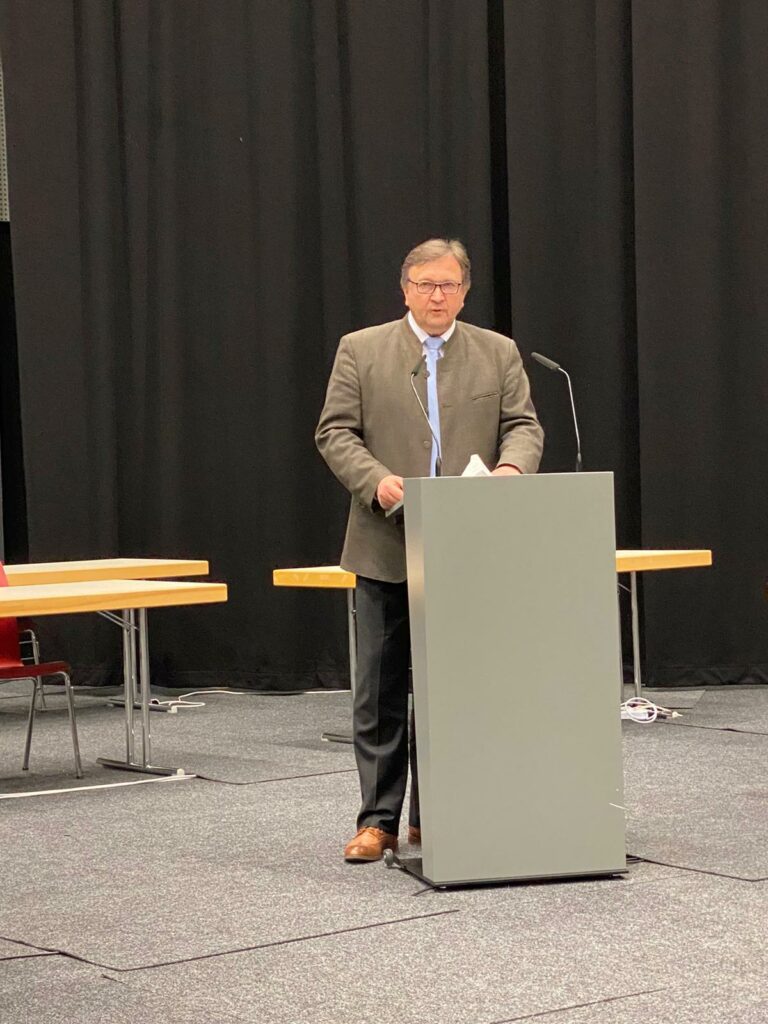 Rudolf Schnur in Anzug und Brille spricht am Rednerpult bei einer Veranstaltung.