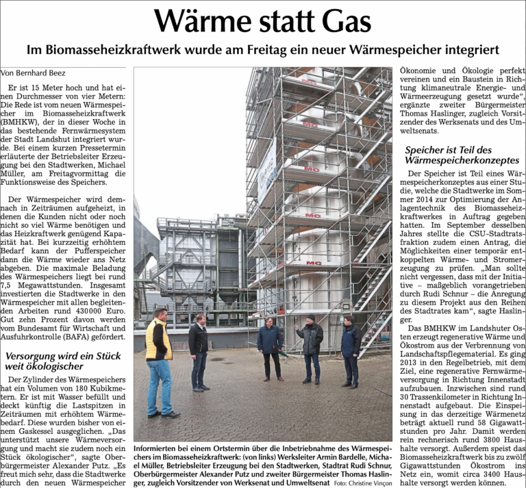 Fünf Personen stehen vor dem neu integrierten Wärmespeicher des Biomasseheizkraftwerks Landshut bei der Inbetriebnahme.